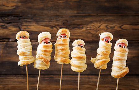 Scary sausage mummies in dough with funny eyes on table.  Halloween food. Top view. Flat layの写真素材