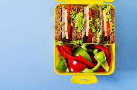 Healthy school lunch box with beef sandwich and fresh vegetables, bottle of water and fruits on blue background. Top view. Flat layの写真素材