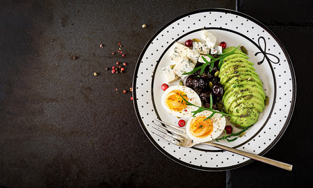 Snack or healthy breakfast  - plate of blue cheese, avocado, boiled egg, olives on a black background. Top viewの写真素材