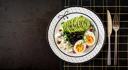 Snack or healthy breakfast  - plate of blue cheese, avocado, boiled egg, olives on a black...