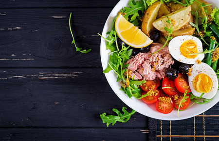 Healthy hearty salad of tuna, green beans, tomatoes, eggs, potatoes, black olives close-up in a bowl on the table. Salad Nicoise. French cuisine. Top view. Flat layの写真素材