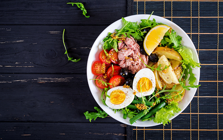 Healthy hearty salad of tuna, green beans, tomatoes, eggs, potatoes, black olives close-up in a bowl on the table. Salad Nicoise. French cuisine. Top view. Flat layの写真素材