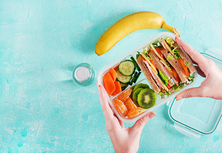 Lunchbox in hands. School lunch box with sandwich, vegetables, water, and fruits on table. Healthy eating habits concept. Flat lay. Top viewの写真素材