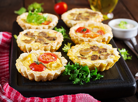 Mushrooms, cheddar, tomatoes tartlets on wooden background. Mini pies. Delicious appetizer, tapas,...