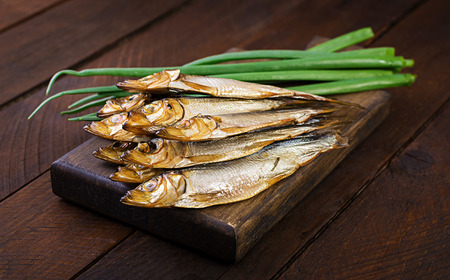 Smoked sprat and green onion  on a cutting board on a wooden background. Smoked fish.