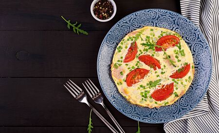 Omelette with tomatoes, ham and green onion on dark table.  Frittata - italian omelet. Top viewの写真素材