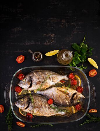 Baked fish dorado with lemon and herbs in baking pan on dark rustic background. Top view. Healthy dinner with fish concept. Dieting and clean eatingの写真素材