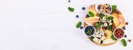 Cheese platter with assorted cheeses, blueberry, apples, nuts on white table. Italian cheese  platter and fruit. Banner. Top view, overheadの写真素材