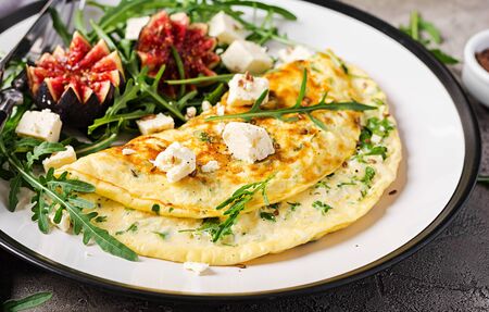 Omelette with feta cheese, parsley and salad with figs, arugula on white plate.