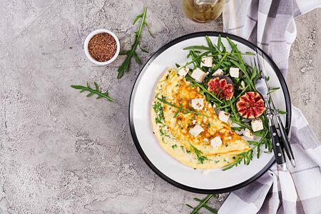 Omelette with feta cheese, parsley and salad with figs, arugula on white plate. Frittata - italian...