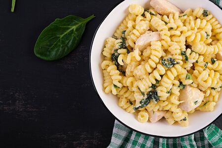 Fusilli pasta with a creamy sauce with chicken meat, parmesan cheese and spinach on a bowl on a dark background.  Top view, copy spaceの写真素材