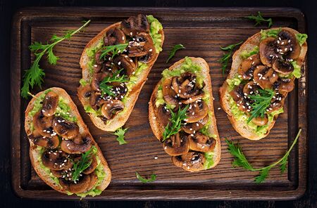 Bruschetta. Sandwich with avocado, fried mushrooms, sesame on a wooden board. Vegetarian food. Vegan menu. Top view, overheadの写真素材
