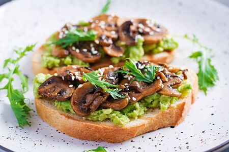 Bruschetta. Sandwich with avocado, fried mushrooms, sesame on a white table. Vegetarian food. Vegan menu.の写真素材