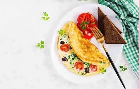 Breakfast. Omelette with tomatoes, black olives, cottage cheese and green herbs on white plate.  Frittata - italian omelet. Top viewの写真素材