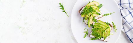 Sandwich of cream cheese bread and slices of avocado on a plate on a light background. Healthy...