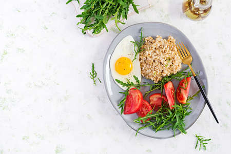 Breakfast oatmeal porridge with fried egg, tomatoes, arugula. Healthy food. Top view, overhead, copy...