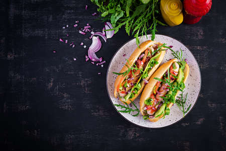 Hot dog with sausage, cucumber, tomato and red onion on dark background. Top view. Flat lay. Copy spaceの写真素材