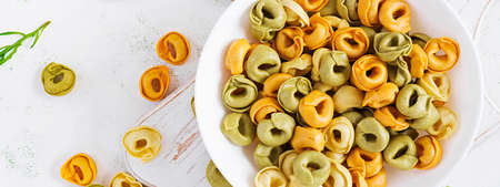 Raw cheese filled tortellini pasta in white bowl. Italian pasta. Top view, banner, overhead