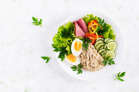 Breakfast oatmeal porridge with boiled egg, ham and vegetables salad. Healthy food. Top view, overhead, copy spaceの写真素材