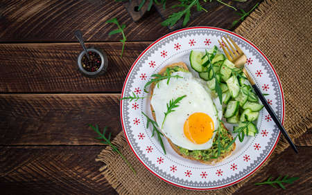 Healthy breakfast. Christmas brunch. Avocado sandwich with fried egg and cucumber with arugula on wooden table. Top view, copy spaceの写真素材