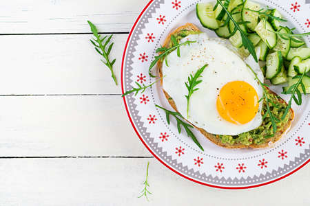 Healthy breakfast. Christmas brunch. Avocado sandwich with fried egg and fresh salad cucumber with arugula for healthy breakfast or snack. Top view, copy spaceの写真素材