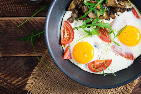 Tasty breakfast - fried eggs, forest mushrooms, tomatoes and arugula. Lunch food. Top view,...