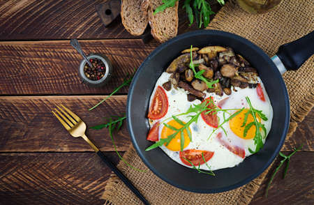 Tasty breakfast - fried eggs, forest mushrooms, tomatoes and arugula. Lunch food. Top view,...