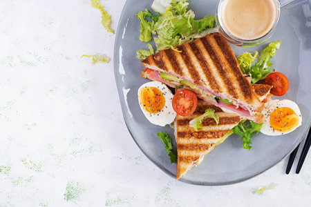 Grilled club sandwich panini with ham, tomato, cheese, avocado and cup of coffee. Delicious breakfast or snack. Top view, flat layの写真素材