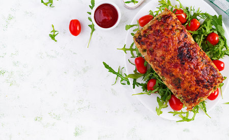Tasty homemade ground baked chicken meatloaf with green peas and sliced broccoli on white table. Food american meat loaf. Top view, overhead, flat layの写真素材