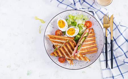 Grilled club sandwich panini with ham, tomato, cheese, avocado and cup of coffee. Delicious breakfast or snack. Top view, flat layの写真素材