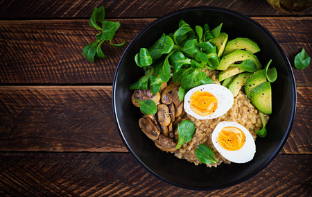 Breakfast oatmeal porridge with boiled egg, avocado and fried mushrooms. Healthy balanced food. Top view, above, copy spaceの写真素材