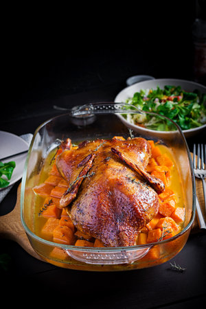 Homemade baked duck. Crispy whole roast duck. Thanksgiving or Christmas dinner. Roast duck with thyme and pumpkin on rustic wooden table.の写真素材