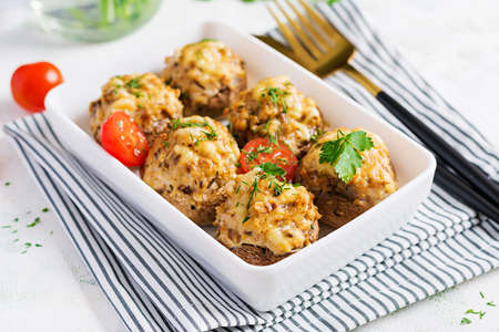 Baked mushrooms stuffed with chicken minced meat, cheese and herbs on light plate.