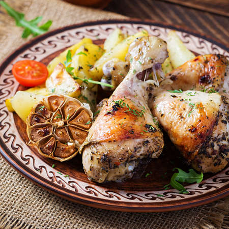 Baked chicken legs with slice potatoes and herbs. Barbecue chicken drumsticks on wooden table.