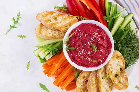 Roasted beet hummus with toast and vegetables on a light background. Beetroot hummus. Top view,...
