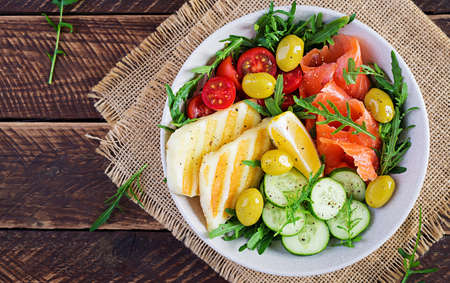 Ketogenic, keto diet. Salted salmon, grilled halloumi cheese, cherry tomatoes and cucumber salad with olives in white bowl. Healthy food. Top view, aboveの写真素材