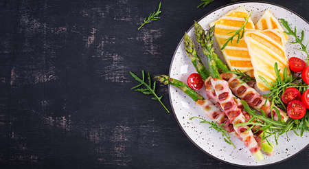 Grilled halloumi cheese salad with tomatoes and asparagus in strips of bacon on plate on dark background. Healthy food. Top view, aboveの写真素材