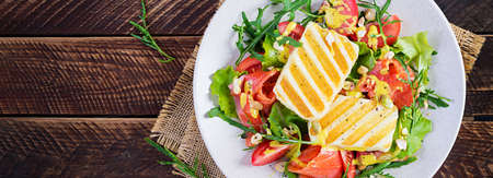 Grilled halloumi cheese salad with salt salmon, tomatoes and green herbs. Healthy food on plate on wooden background. Top view, bannerの写真素材