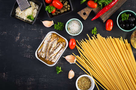 Ingredients for cooking pasta spaghetti alla puttanesca - italian pasta dish with tomatoes, black olives, capers, anchovies and parsley. Top view, flat layの写真素材