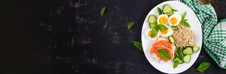 Breakfast oatmeal porridge with boiled eggs, salmon sandwich and cucumbers salad. Healthy food. Lunch. Top view, banner, flat layの写真素材