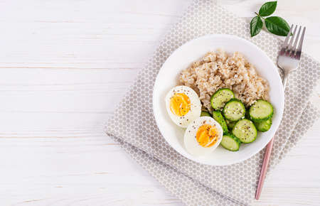 Breakfast oatmeal porridge with boiled egg, cucumber and sesame seed. Healthy balanced food. Top view, flat layの写真素材