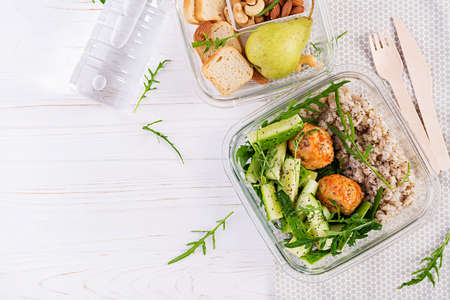 Lunch box filled with oatmeal, cucumber salad, and nuts, bread, pear on white wooden background. Lunchbox dinner. Top view, flat layの写真素材