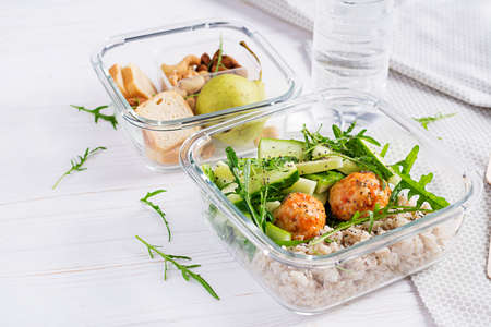 Lunch box filled with oatmeal, cucumber salad, and nuts, bread, pear on white wooden background. Lunchbox dinner.の写真素材