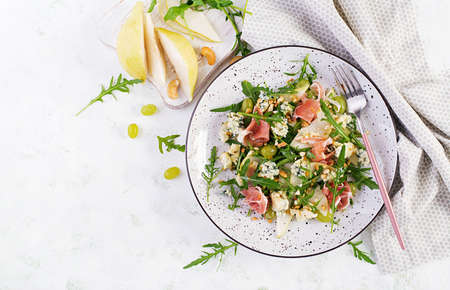 Salad of pear, blue cheese, grape, prosciutto, arugula and nuts with spicy dressing on a light background. Healthy eating. Top view, overheadの写真素材