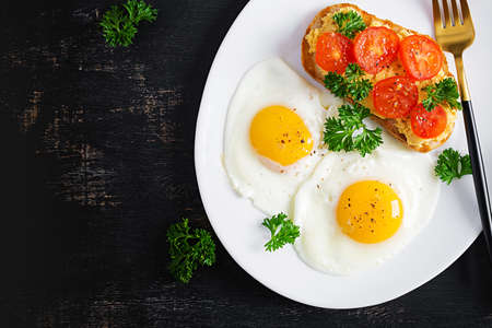 Fried eggs and a grilled chicken pate  sandwich on a dark background. Top view, overhead