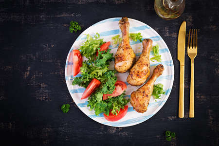 Baked chicken drumsticks and fresh salad on a dark background. Top view, flat layの写真素材