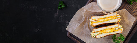 Roasted sandwich cheese and scrambled eggs on paper with coffee glass cup on wooden board. Dark background. Top view, aboveの写真素材