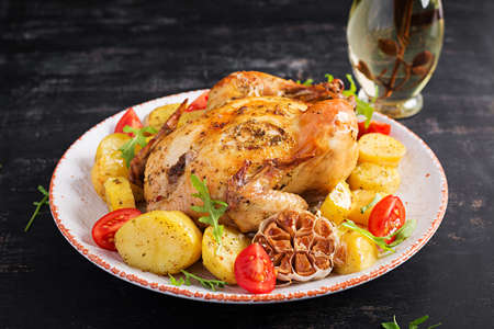 Baked chicken with potatoes in a white plate. Dark background.の写真素材