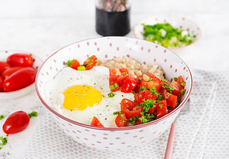Breakfast oatmeal porridge with roasted egg and tomatoes salad. Healthy balanced food.の写真素材