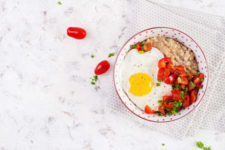 Breakfast oatmeal porridge with roasted egg and tomatoes salad. Healthy balanced food. top view,...